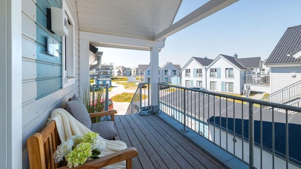 Ein Balkon mit Blick auf ein Wohngebiet, ein Holzstuhl und ein Geländer.