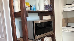Une cuisine équipée d’une étagère en bois où sont rangés les ustensiles de cuisine, d’un four à micro-ondes et d’une cuisinière.