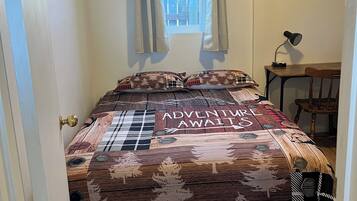 Une chambre à coucher avec un lit agrémenté d’une couvre-lit sur le thème « L’aventure vous attend », une fenêtre avec des rideaux, un bureau avec une lampe et une chaise.