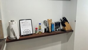 A kitchen shelf with a menu, a bottle of olive oil, a box of tea, wooden utensils, and a knife block.
