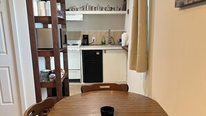 Un coin repas avec une table ronde en bois et des chaises, une cuisine à l’arrière-plan et un tableau accroché au mur.