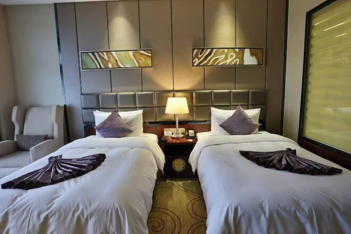 A hotel room with two beds, a nightstand, a lamp, and a chair.