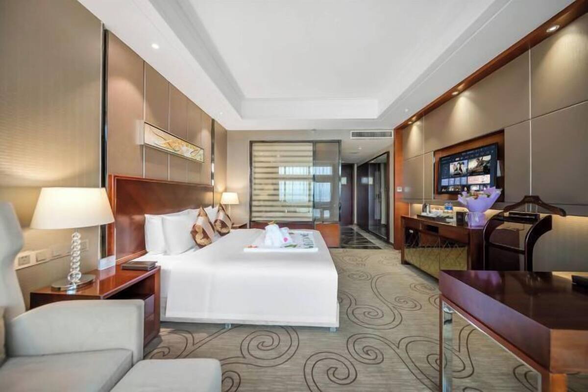 A hotel room with a bed, bedside tables, a desk, a TV, and a view of the hallway.