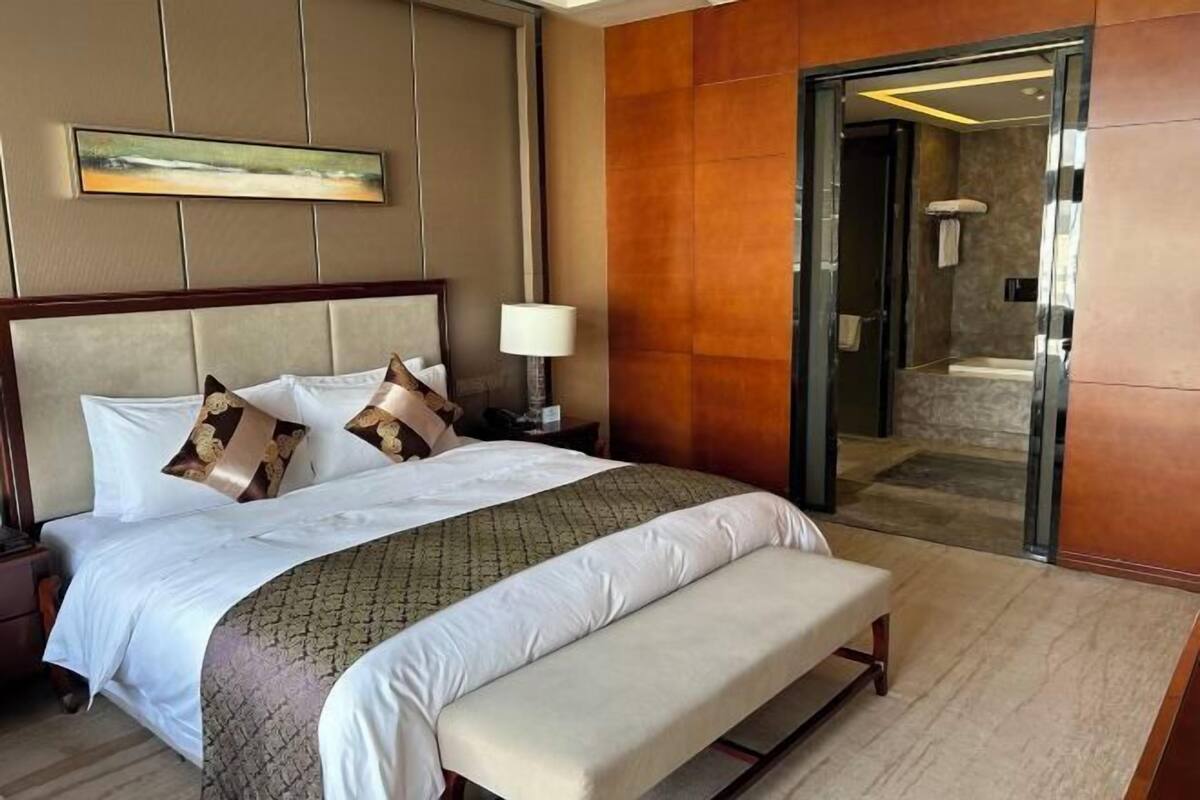 A hotel room with a large bed, a bedside table, a lamp, and a view of the bathroom.