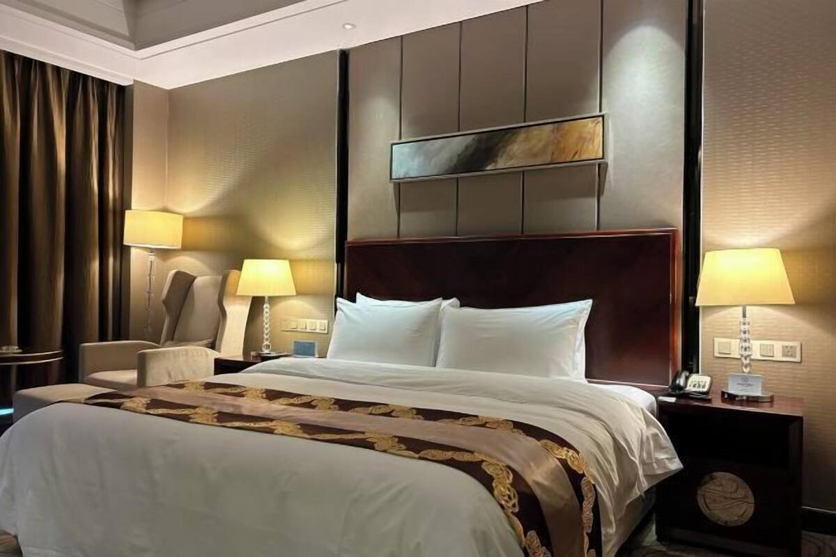 A hotel room with a large bed, two bedside tables with lamps, a chair, and a clock on the wall.