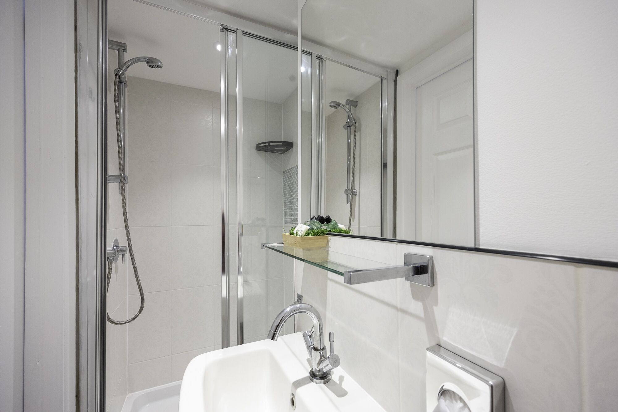 A modern bathroom with a glass-enclosed shower, a white sink, and a mirror above the sink.