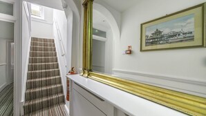 Una escalera con alfombra a rayas, un espejo grande con marco dorado y un cuadro enmarcado en la pared.