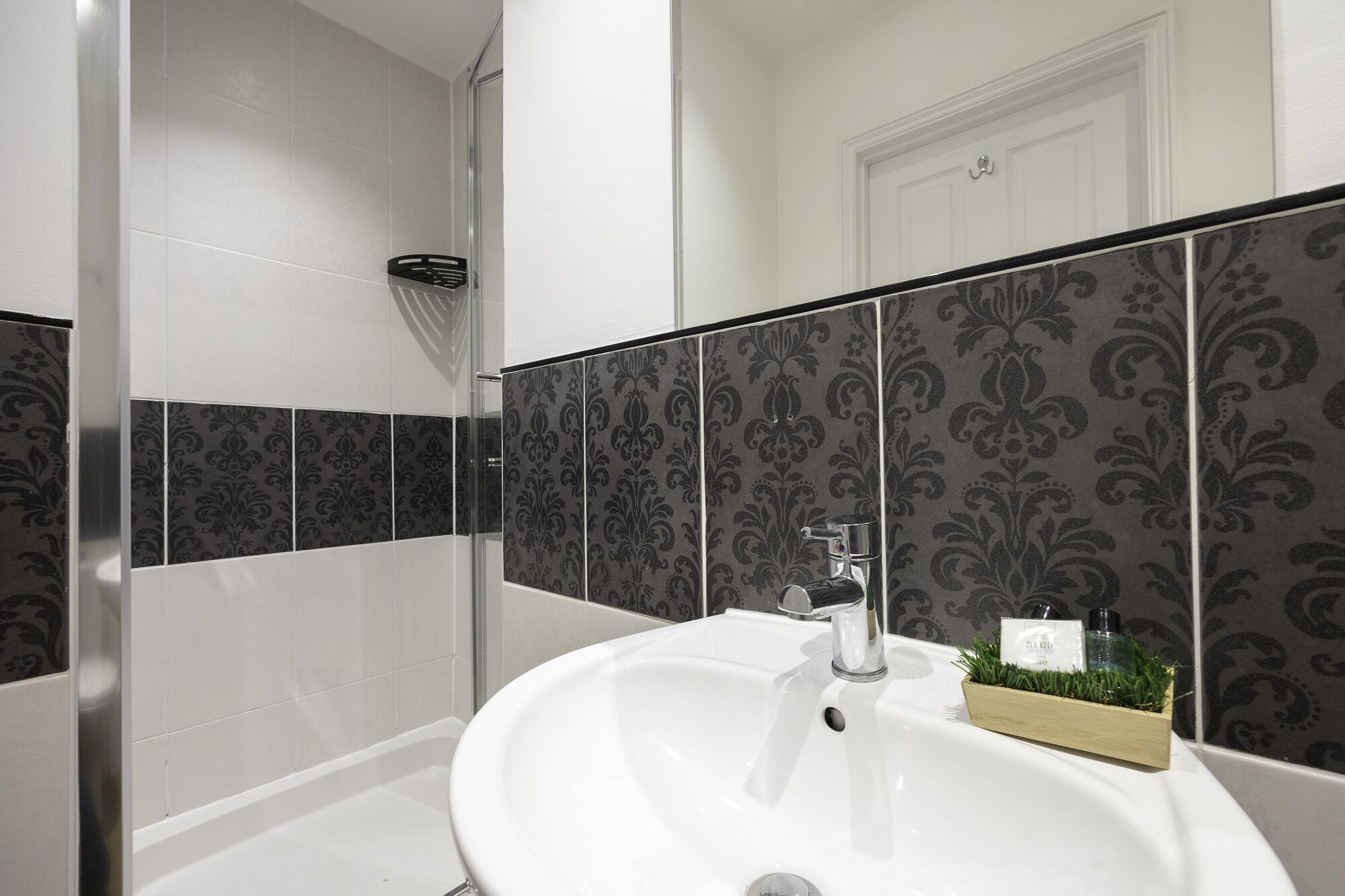 A bathroom with a white sink, a shower, and patterned tiles.