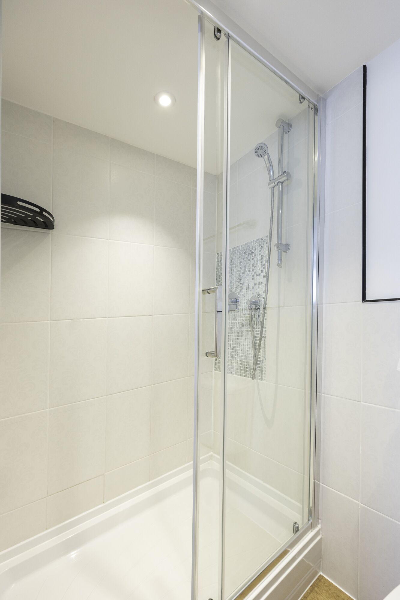 A glass-enclosed shower with a handheld showerhead and a wall-mounted faucet.