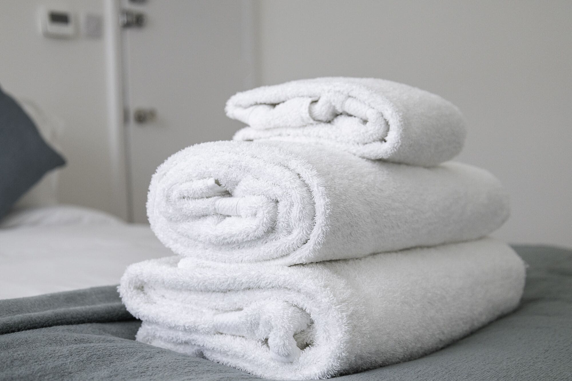 Een stapel witte handdoeken op een bed met een grijze deken.
