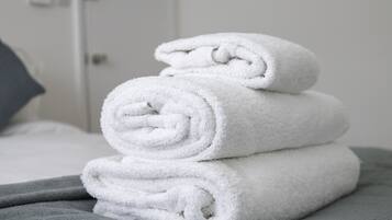 Een stapel witte handdoeken op een bed met een grijze deken.