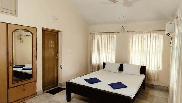 A bedroom with a bed, a wardrobe, a ceiling fan, and curtains. - NuaGoa Nature Retreat Private Limited (Cuttack)