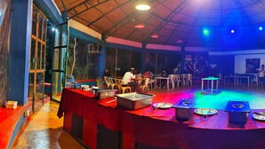 A restaurant with a high ceiling and a stage for performances. Tables are arranged around the stage, and there are food service stations in the center. - NuaGoa Nature Retreat Private Limited (Cuttack)
