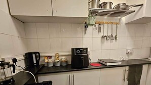 A kitchen with white cabinets, a black countertop, a coffee maker, and a kettle. - Tropical Hideaway Studio Apartment (Cardiff)