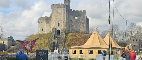 A castle with a tower, surrounded by a fenced area with tents and a signboard.