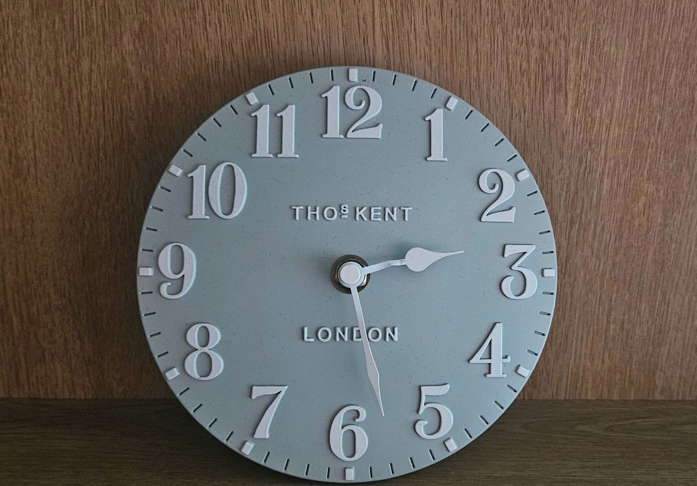 Une horloge THOS KENT de Londres avec un fond en bois.