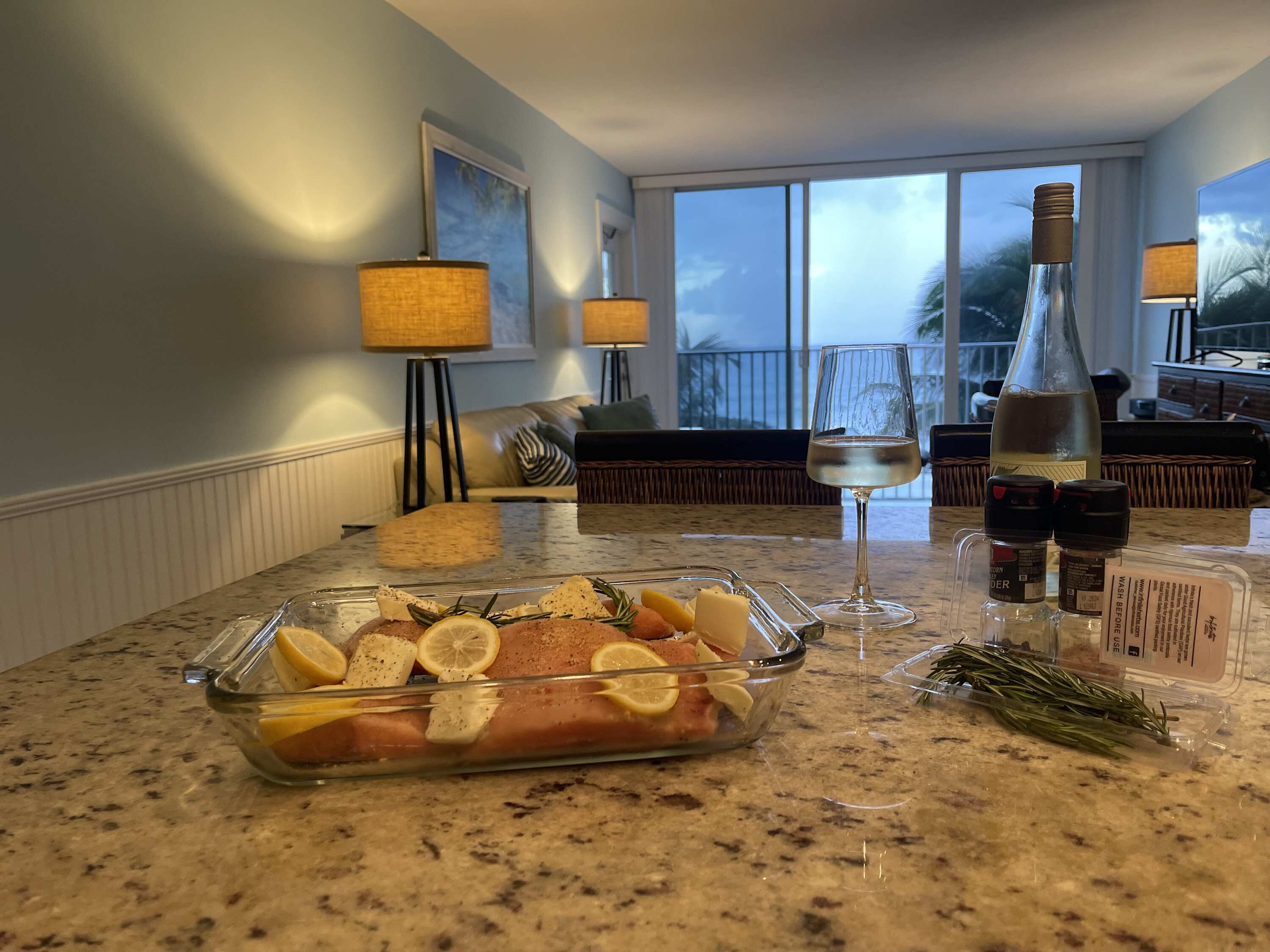A kitchen counter with a glass dish containing food, a wine glass, and a bottle.