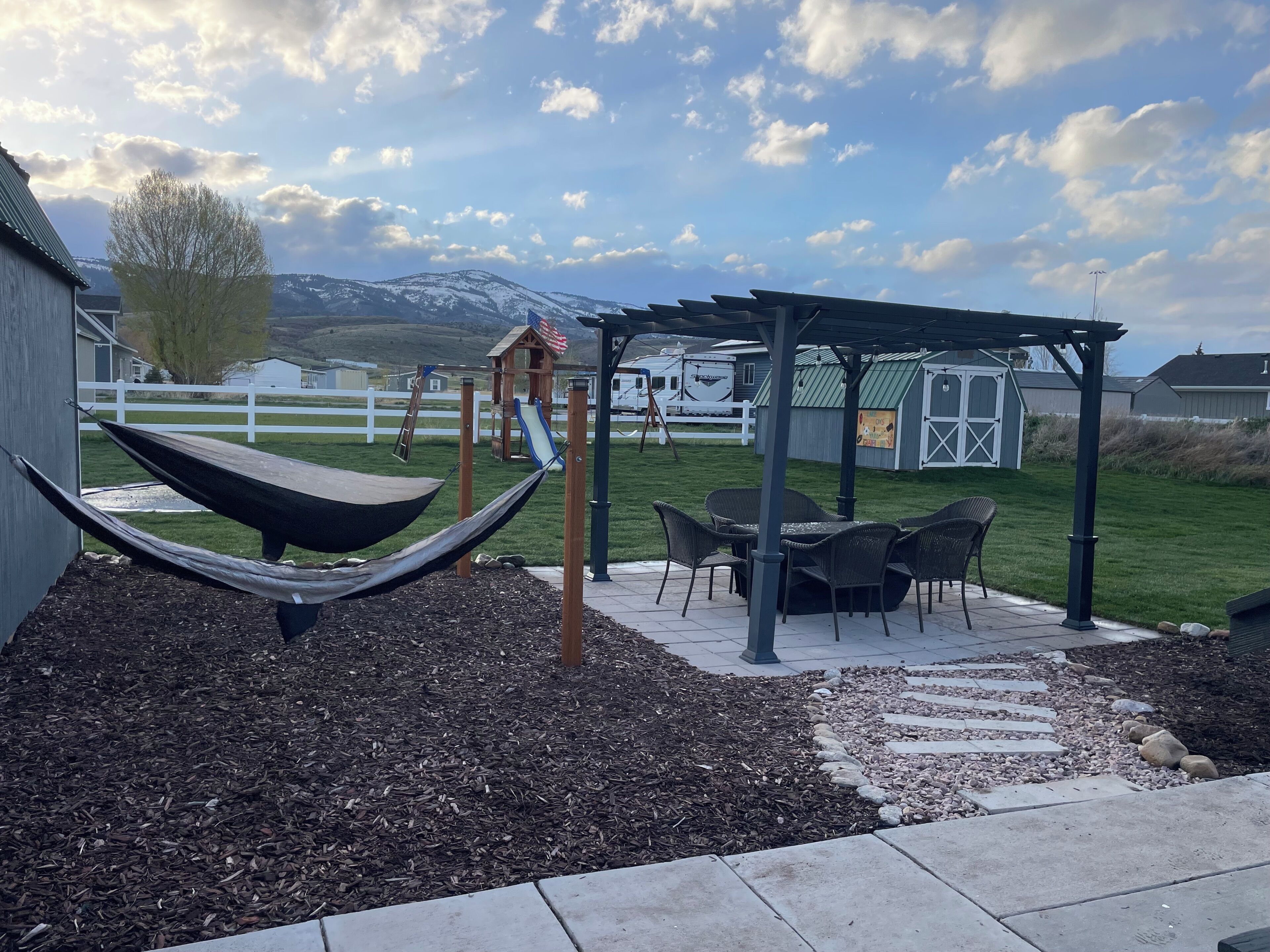 A backyard with a hammock, patio furniture, a play structure, and a pergola.