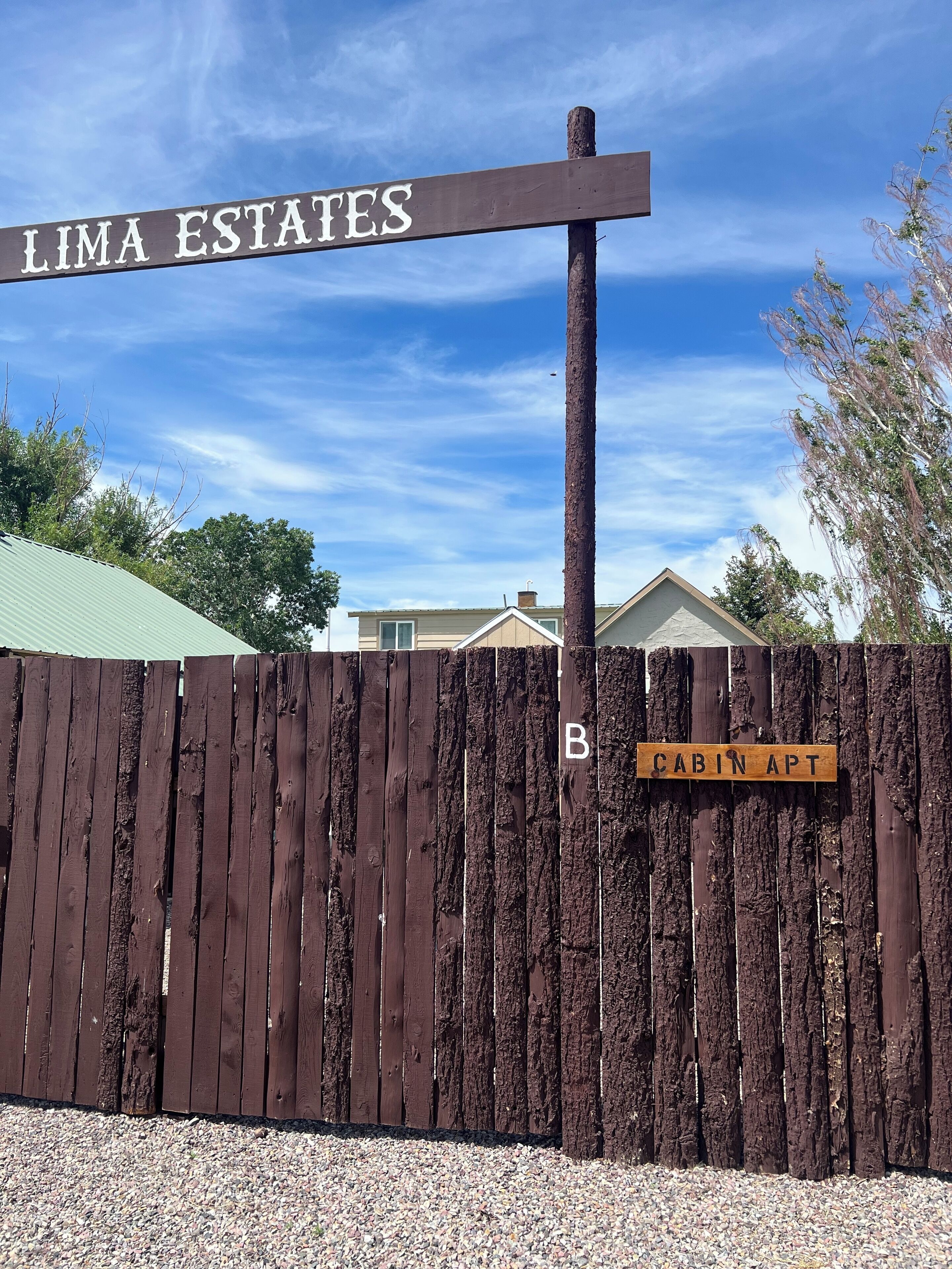A wooden fence with a sign that reads "LIMA ESTATES" and another sign below it that says "CABIN APT".