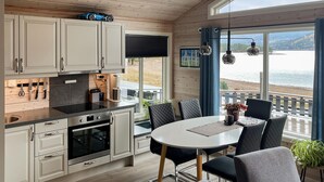 Et moderne køkken med hvide skabe, en sort bordplade og rustfrie stålemmer. Der er et spiseområde med et rundt bord og sorte stole. En blå bil er parkeret udenfor vinduet.
