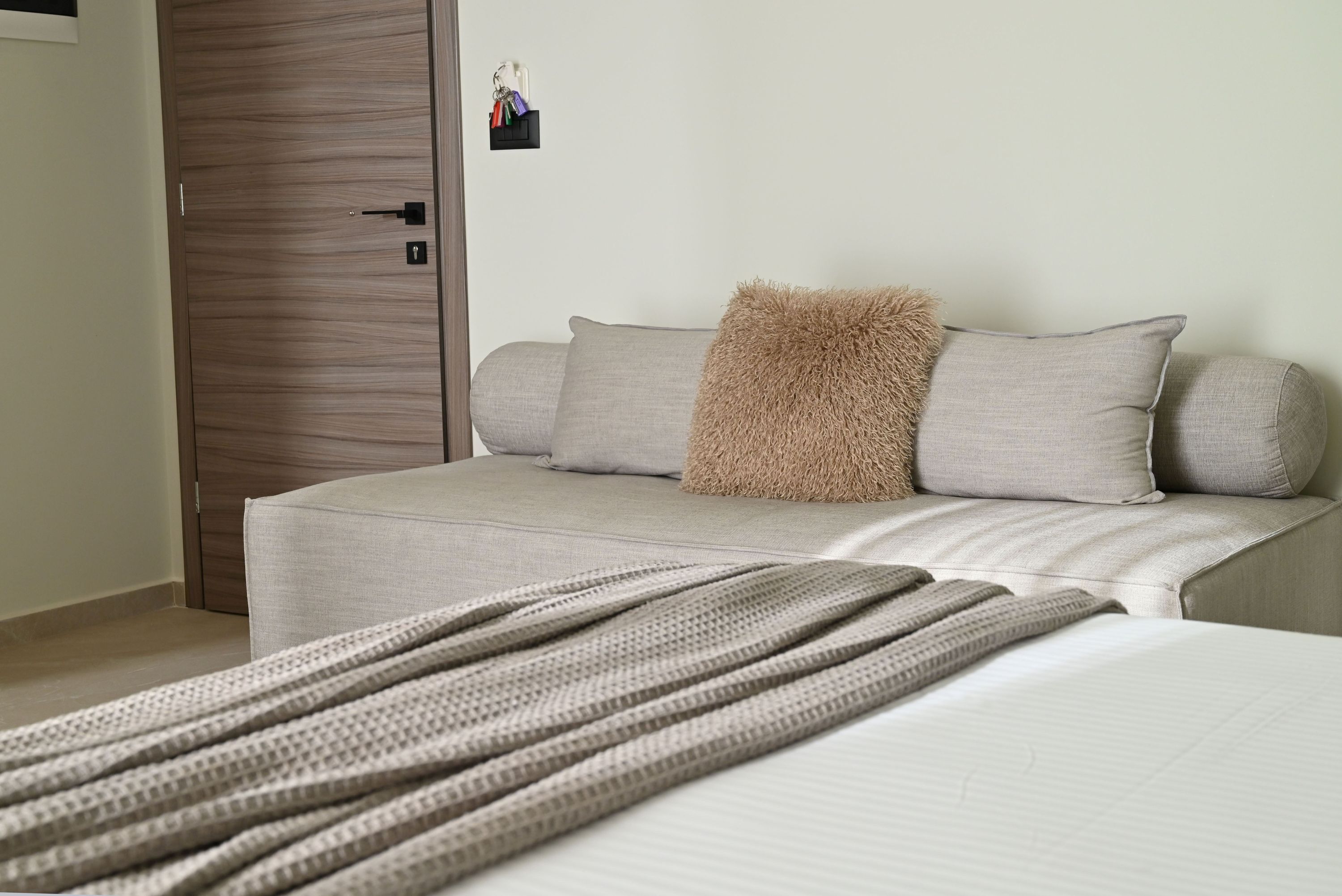 Ein Schlafzimmer mit einem Bett, einem grauen Sofa, einem kuscheligen Zierkissen und einem Schlüsselhalter an der Wand.