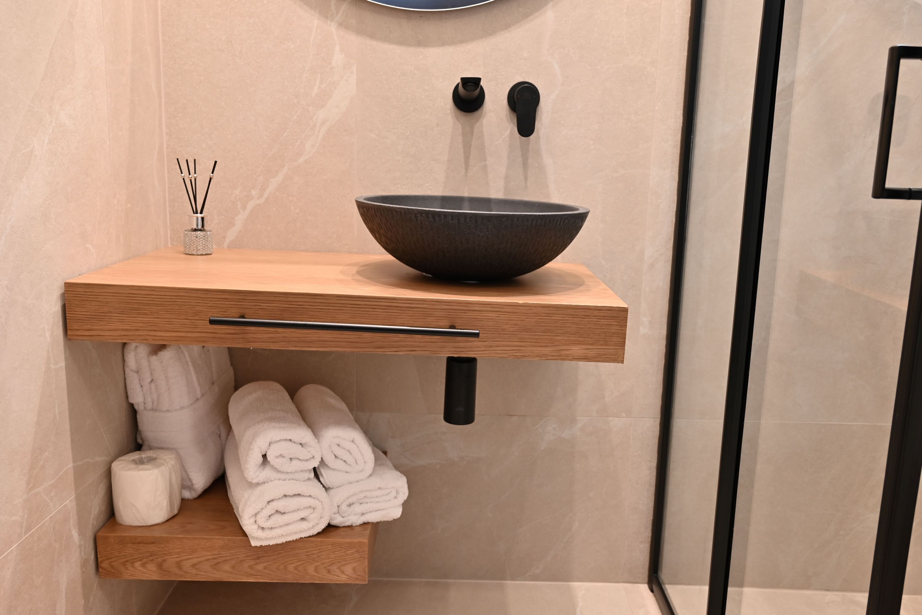 Une salle de bain moderne avec un meuble-lavabo en bois, un lavabo noir et des serviettes soigneusement pliées.