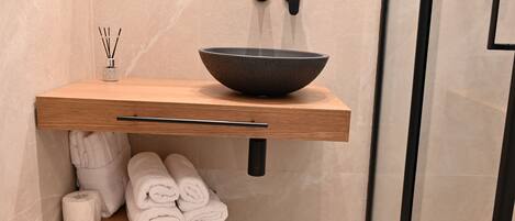 Une salle de bain moderne avec un meuble-lavabo en bois, un lavabo noir et des serviettes soigneusement pliées.