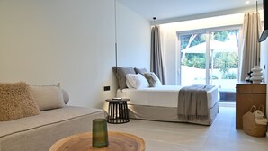 Ein modernes Schlafzimmer mit einem Bett, einem Sofa, einem kleinen runden Holztisch und einem Fenster mit Vorhängen.