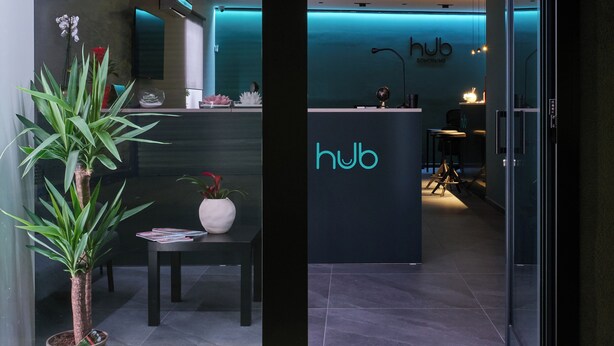 A modern coworking space with a reception desk, a potted plant, and a glass partition. - HUB Rooms (Carini)