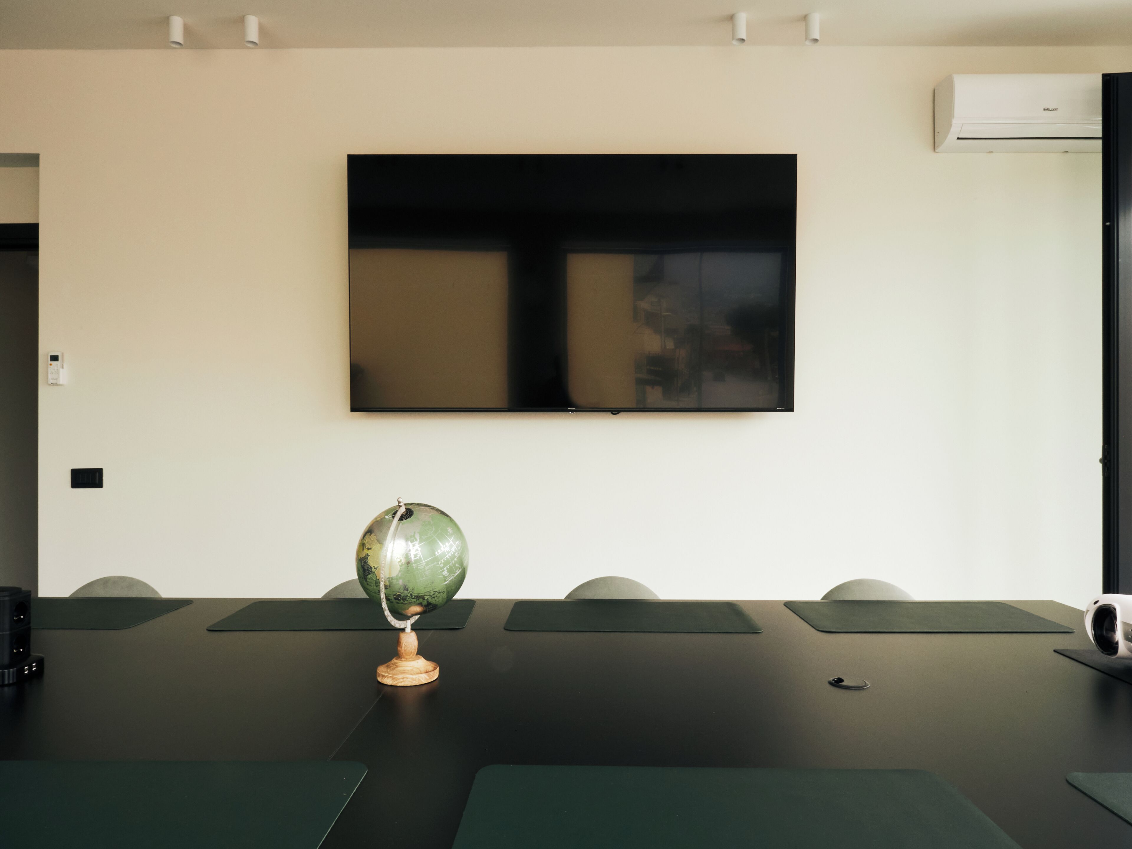 A conference room with a large flat-screen TV mounted on the wall, a wooden globe on a table, and several green mats on the floor.