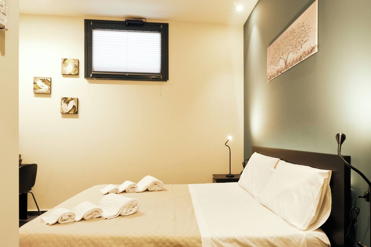 A neatly made bed with rolled towels, a bedside lamp, and a window with blinds.