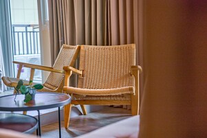 Una silla de mimbre con asiento y respaldo acolchados, ubicada junto a una pequeña mesa redonda con un florero de plantas verdes.