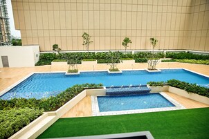 Una piscina con varias pistas, rodeada de jardines verdes y un muro color beige.