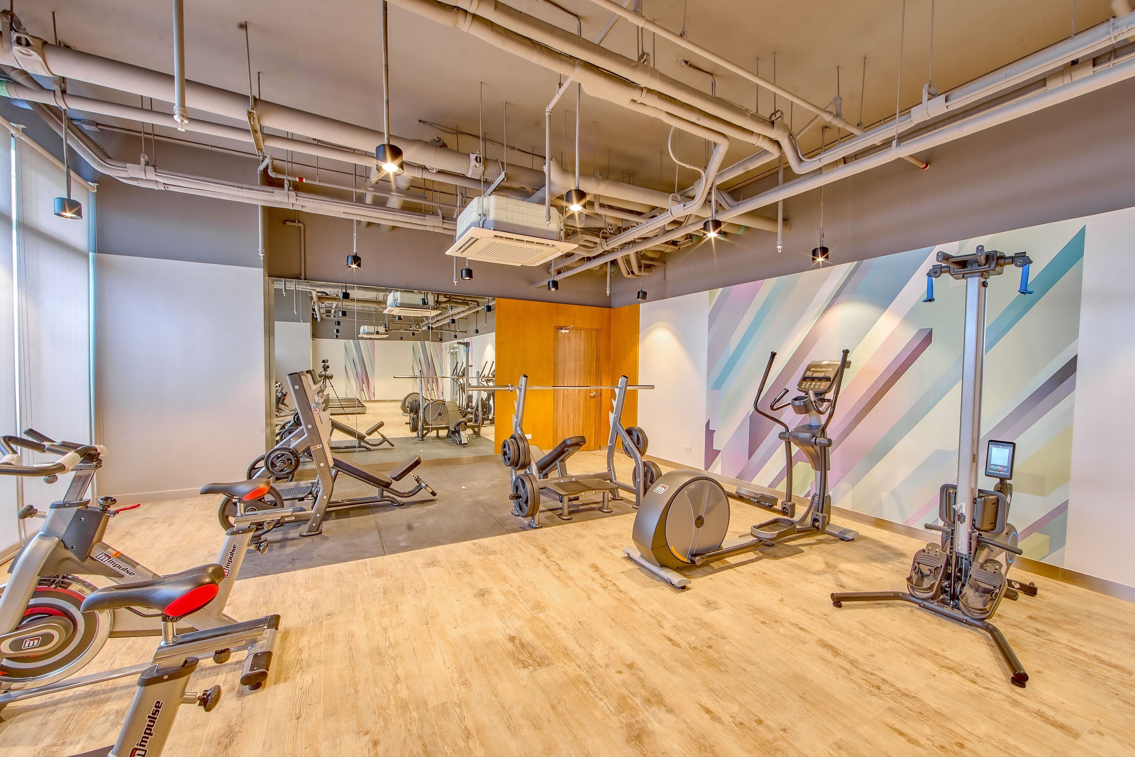Un gimnasio con equipo de ejercicio diverso, incluyendo bicicletas estáticas y máquinas de pesas, y suelo de madera.