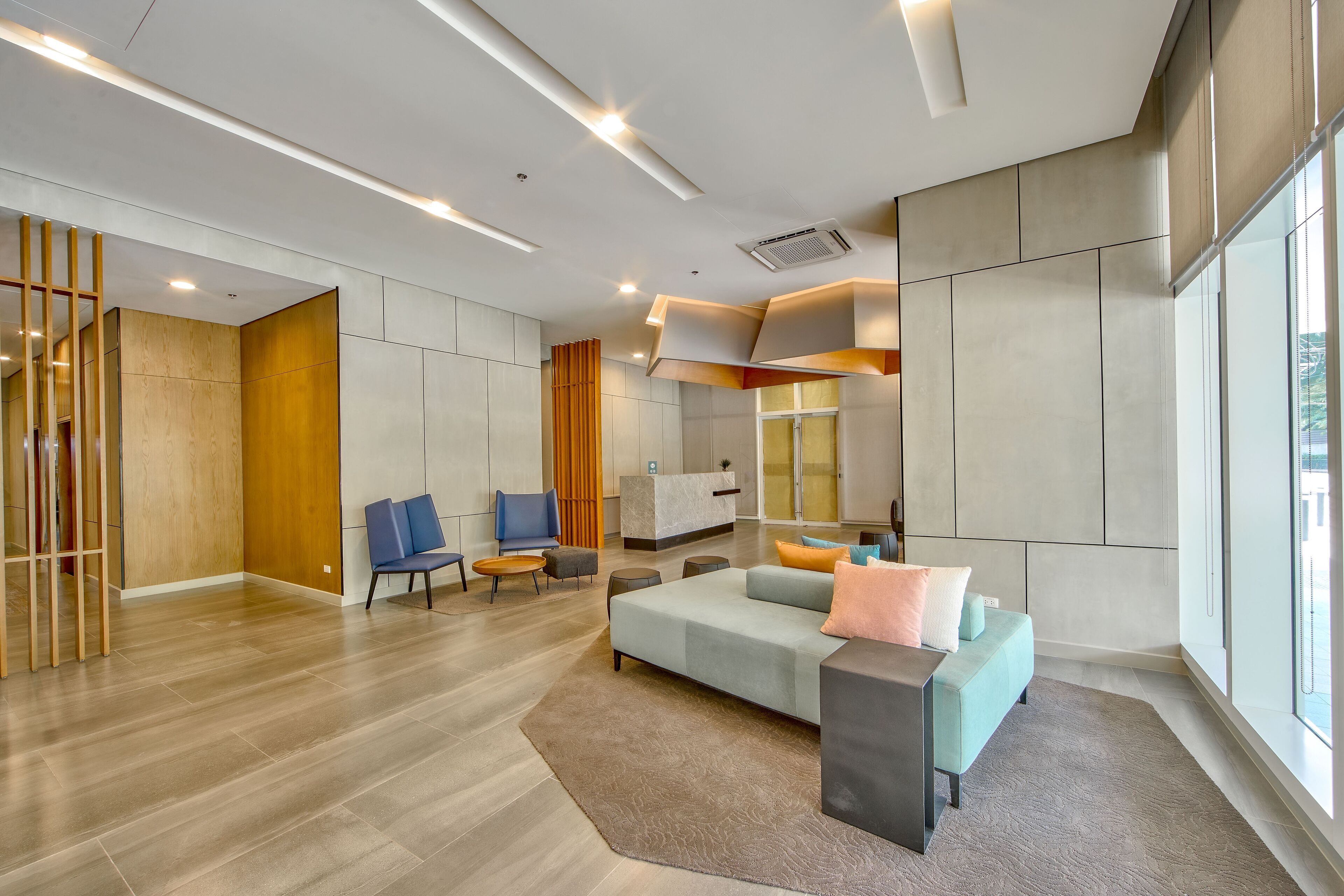 A modern hotel lobby with a seating area, a reception desk, and large windows.