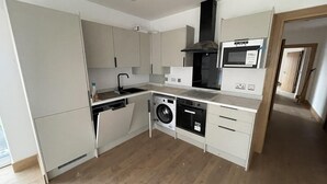 A compact kitchen with a built-in washer and dryer, a microwave, and a stove. - Exquisite Riverside Living in a Stunning Flat (Gravesend)