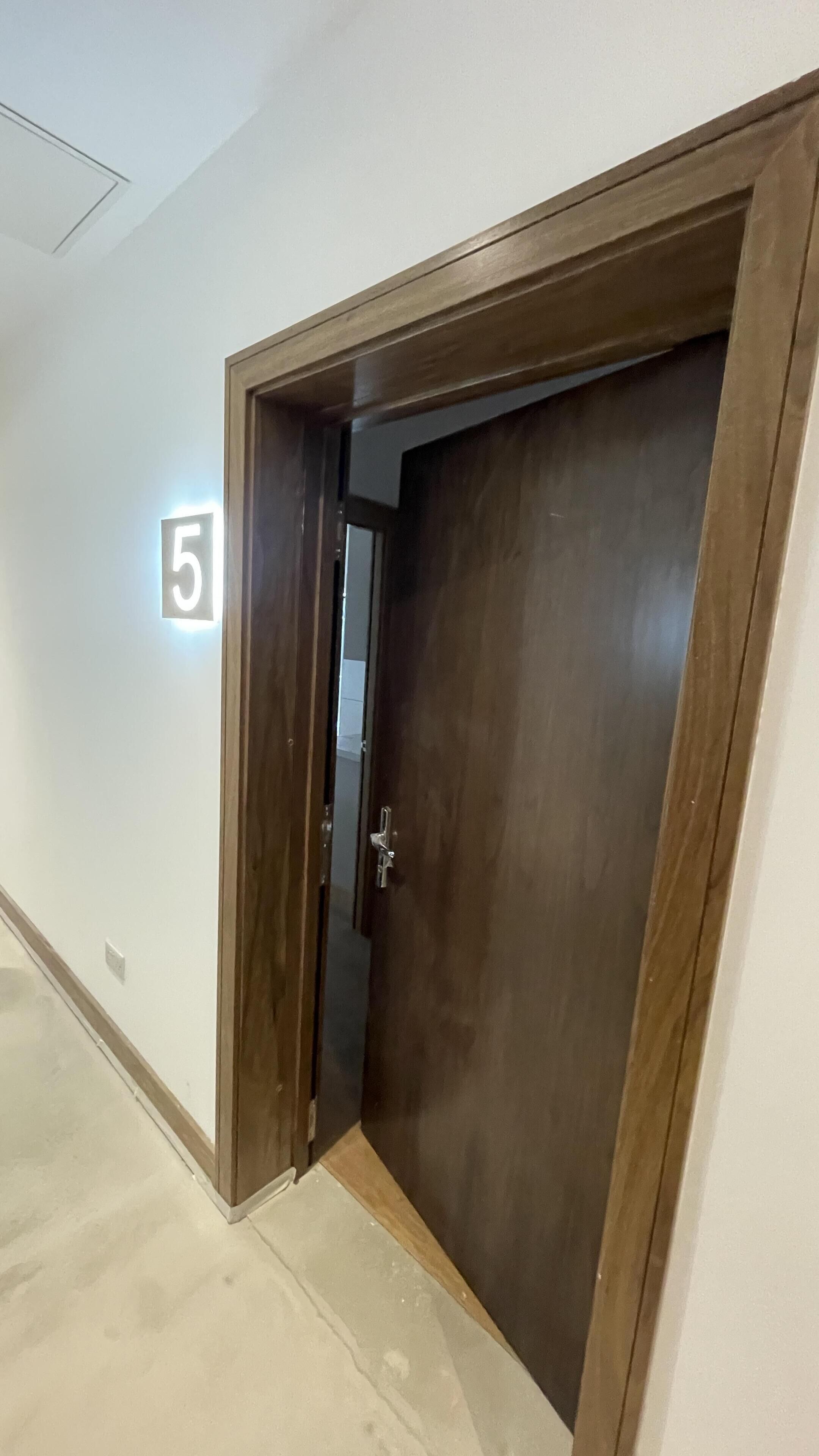 A hallway with a wooden door, a number '5' sign, and a light switch on the wall.