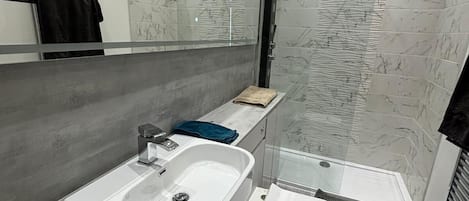 A modern bathroom with a white sink, a glass shower enclosure, and a marble backsplash.