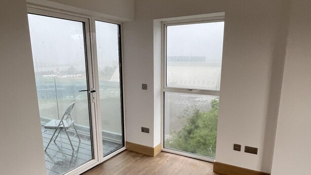 A spacious room with large windows, wooden flooring, and a view of a body of water. - Exquisite Riverside Living in a Stunning Flat (Gravesend)
