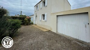 A two-story building with a garage, a gravel driveway, and a garden with pink flowers.