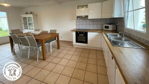 A kitchen with white cabinets, a microwave, and a sink. There is a dining table with chairs and a cabinet with glass doors.
