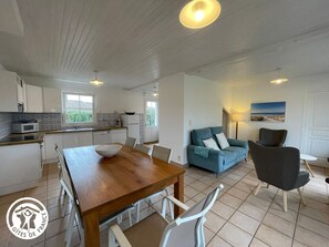 A modern kitchen with white cabinets and a wooden dining table. There is a blue sofa and a black armchair in the living area. - Charming 6-Person Cottage Near Beaches and Cycling Paths in Talmont St Hilaire (Talmont-Saint-Hilaire)