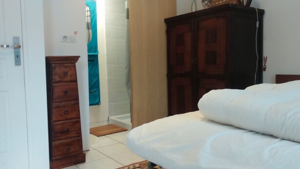 Ein Schlafzimmer mit Bett, Holzschrank und Badezimmer, im Badezimmer hängt ein Handtuch an der Wand.