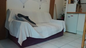 Ein Zimmer mit einem weißen Sofa, das mit Stoff bedeckt ist, einem kleinen weißen Kühlschrank und einem Holzstuhl.