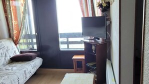 A compact room with a bed, a small desk, a chair, and a television. - Appartement 6 Couchages 1800m d Altitude (Bagnères-de-Luchon)