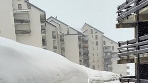 A snowy residential street with parked cars and multi-story buildings in the background. - Appartement 6 Couchages 1800m d Altitude (Bagnères-de-Luchon)