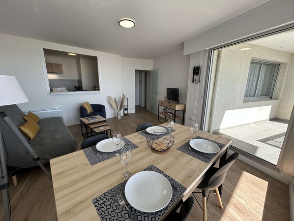 En moderne stue med spiseplads, sofa, fjernsyn og et stort vindue.