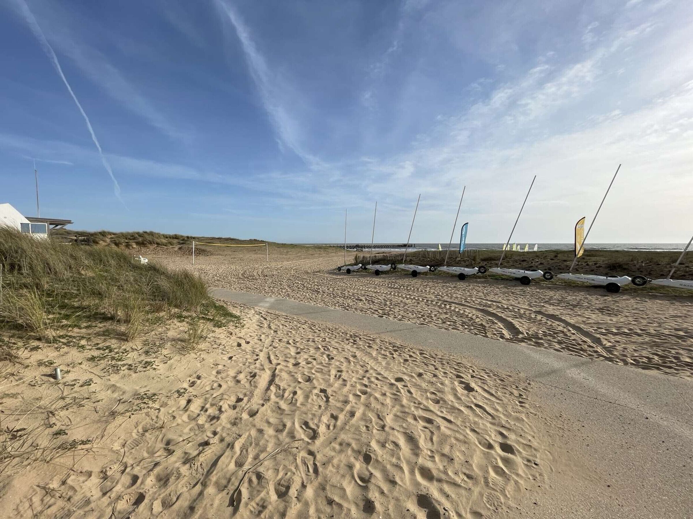 Een zandstrand met windsurfuitrusting en een klein gebouw.