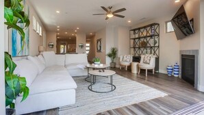 A modern living room with a white sofa, two round coffee tables, a ceiling fan, and a fireplace. - Ocean-View Home Blocks to Beach with Private Hot Tub & Rooftop Deck! (San Diego)