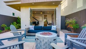 An outdoor seating area with Adirondack chairs, a stone fire pit, and a blue sofa with cushions. - Ocean-View Home Blocks to Beach with Private Hot Tub & Rooftop Deck! (San Diego)